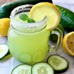Refreshing cucumber lemonade garnished with lemon and cucumber slices on a sunlit table.